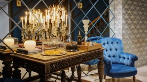 A room with a blue armchair, a table with books and a decorative glass dome, and a chandelier.
