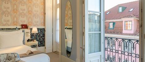 Una habitación de hotel con cama, mesita de noche, lámpara y un espejo grande.