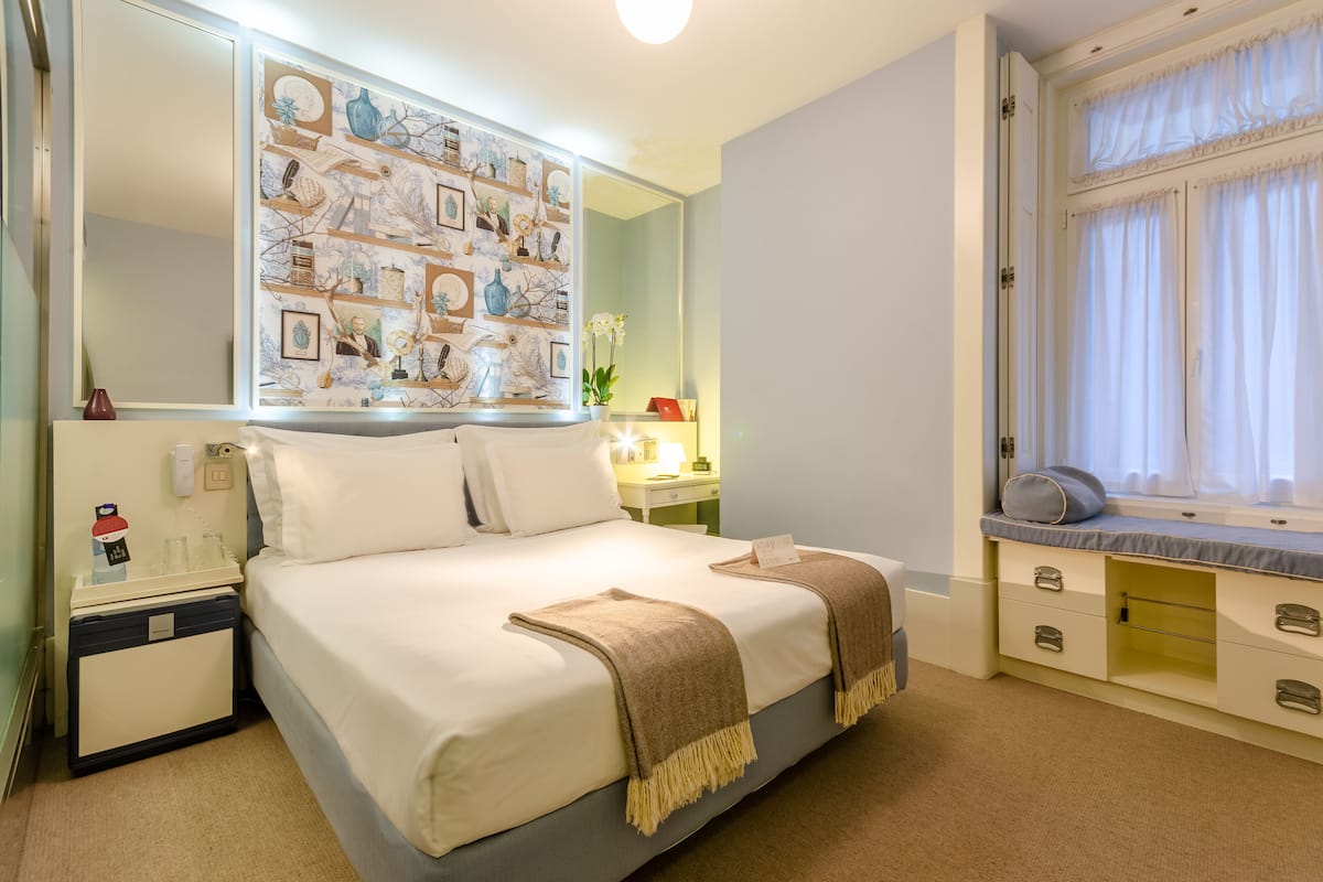 Een opgemaakt bed met een beige deken, een nachtkastje met een lamp, en een muur versierd met ingelijste foto's.