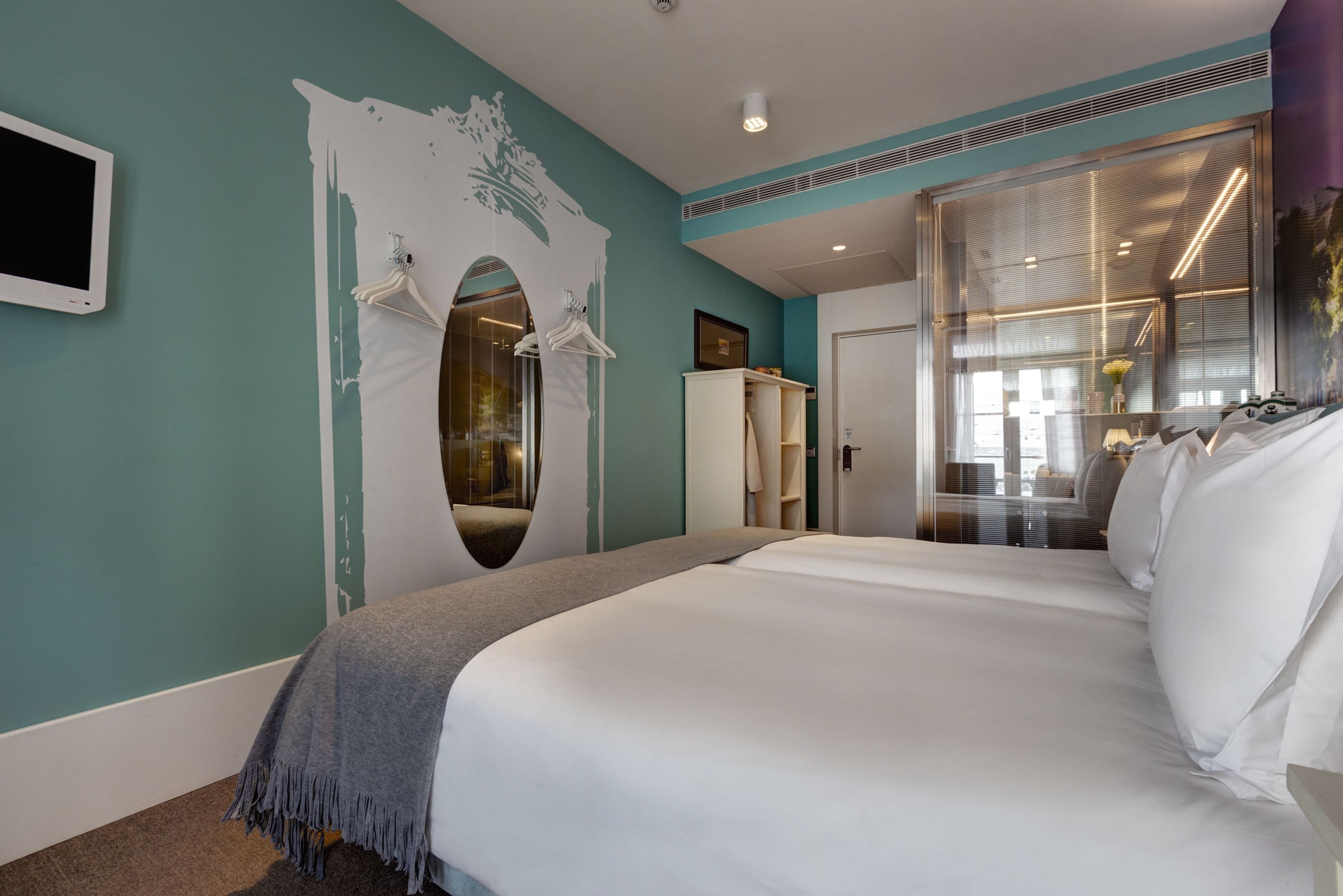 A modern hotel room with a large bed, a wardrobe, a mirror, and a view of the outside.