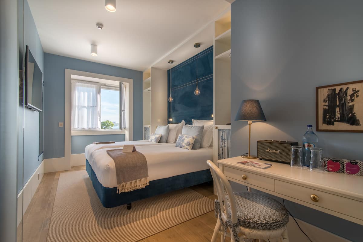 Een slaapkamer met een bed, nachtkastje, lamp en bureau met stoel.