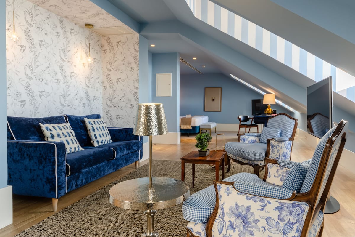 Een moderne woonkamer met een blauwe bank, gestreept fauteuils, een ronde tafel en een trap naar een hoger niveau.