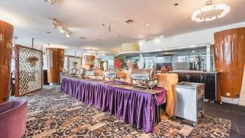 A hotel dining area with a long table, chairs, and a buffet setup.