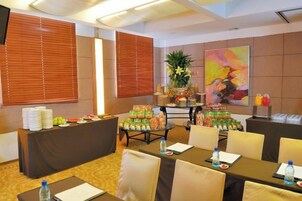 Un salón de conferencias con una larga mesa, sillas, una mesa de buffet con comida y bebidas, y un cuadro grande en la pared.