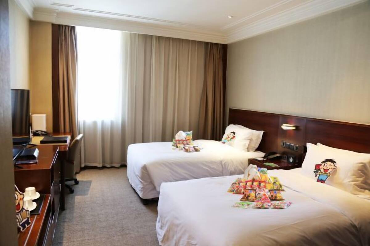 A hotel room with two beds, a desk, and a TV.