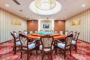 Un salón de conferencias con una mesa redonda, sillas, un televisor de pantalla plana y paneles decorativos en la pared.