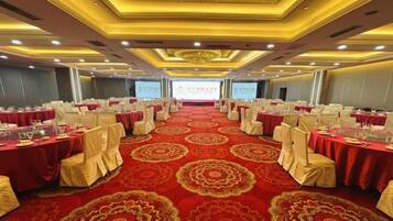 A banquet hall with round tables, red carpet flooring, and a large screen at the front.