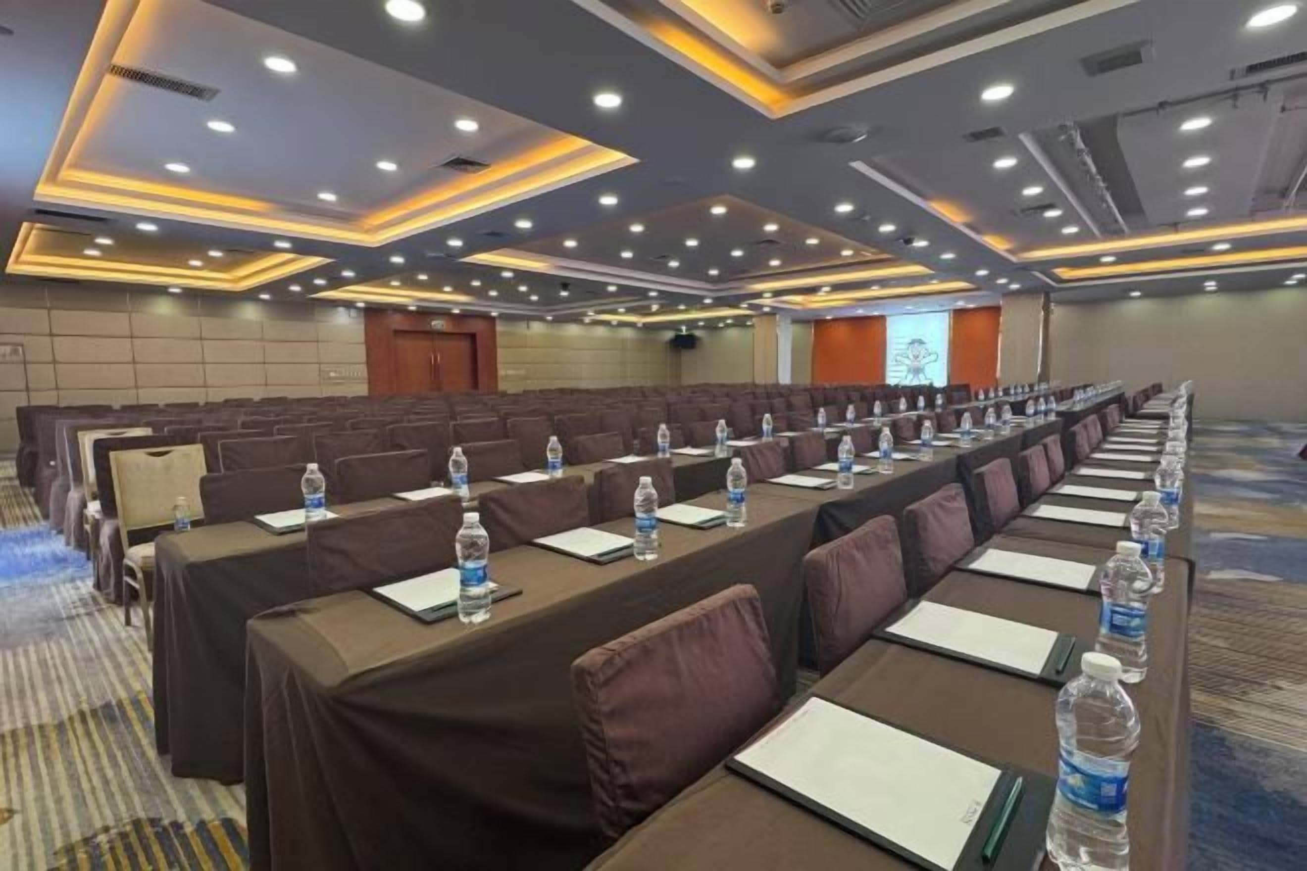 A conference room with rows of tables, each equipped with water bottles and notepads.