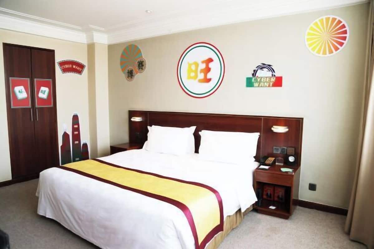 A hotel room with a large bed, a wooden headboard, a nightstand with a lamp, and a wall with various signs and logos.