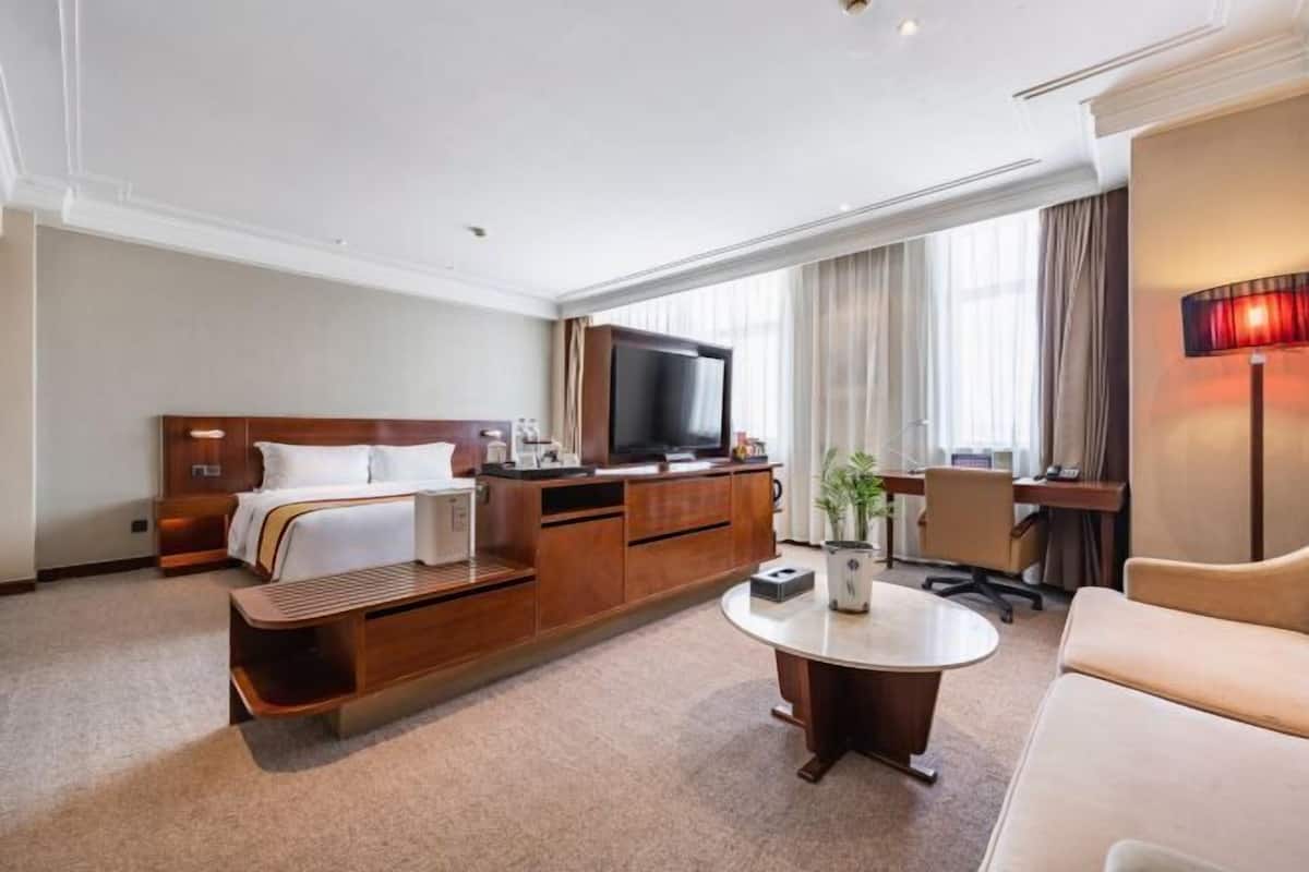 A hotel room with a bed, a TV, a desk, a chair, and a coffee table.