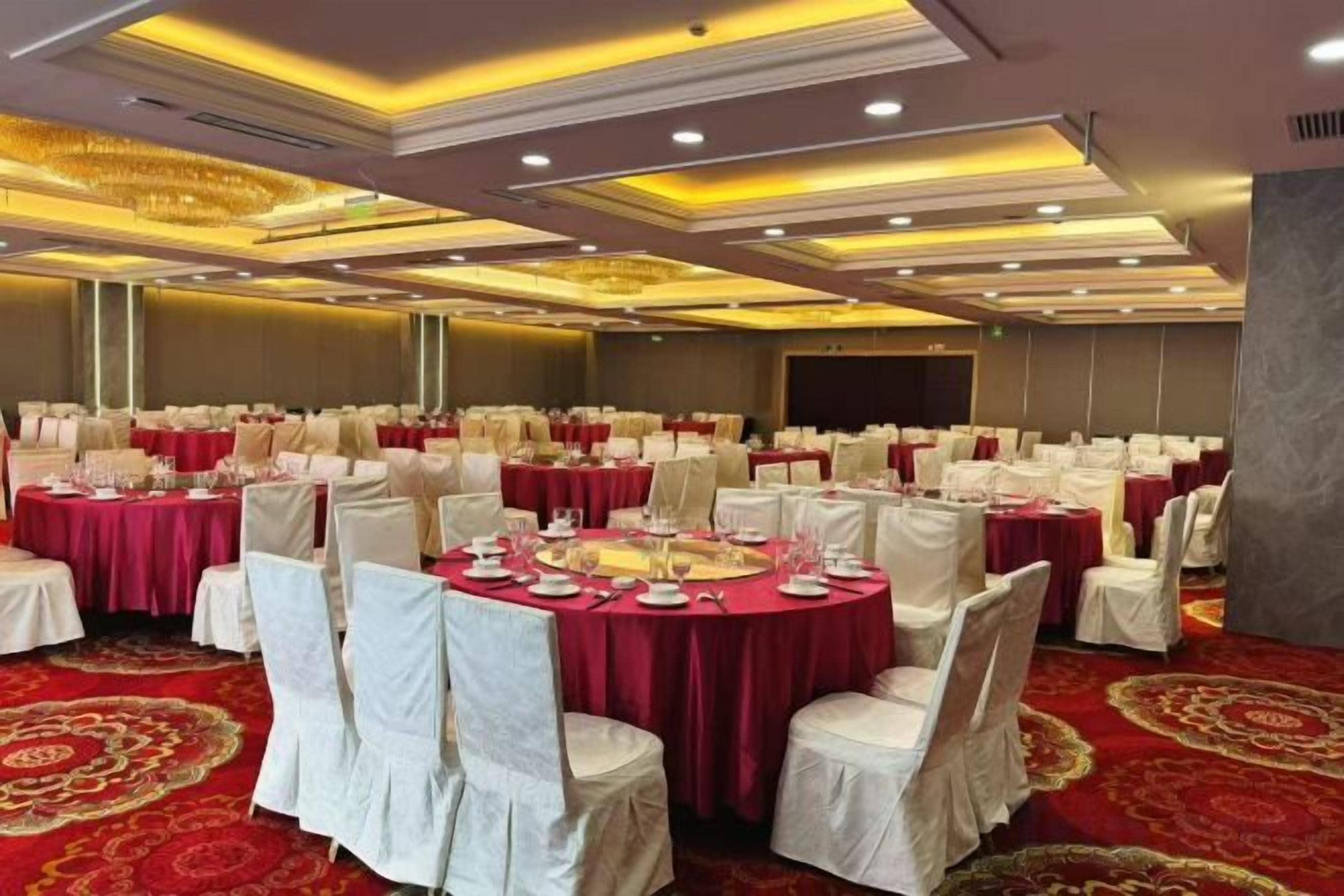 Une salle de banquet avec des tables rondes, des chaises blanches et une moquette rouge.