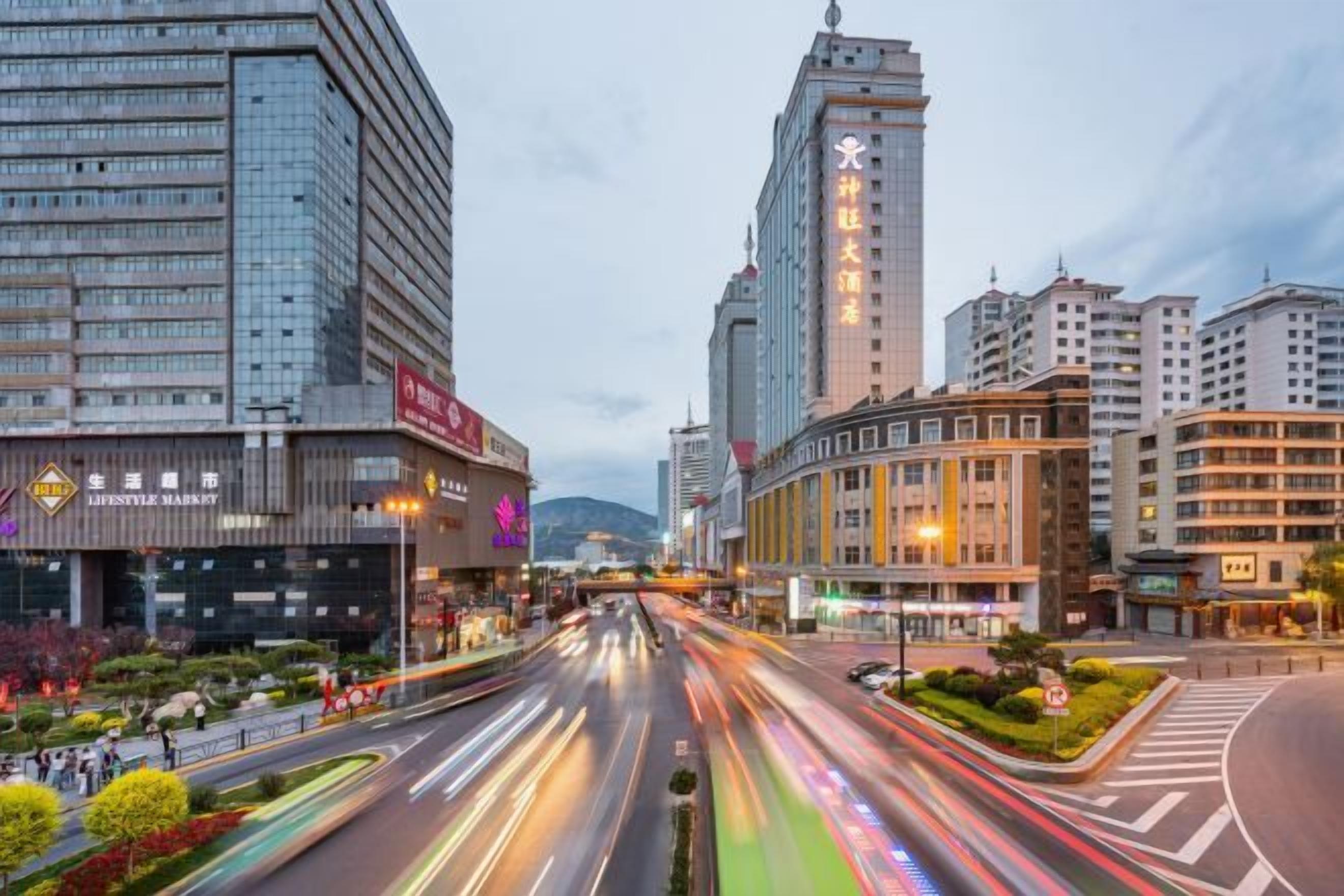 A city street with modern buildings, a busy road, and a clear sky.