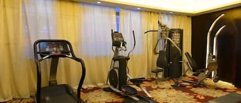 Gimnasio de hotel con cinta de correr, elíptica y máquina de pesas.