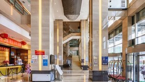A modern hotel lobby with a reception desk, a staircase, and a glass elevator. - San Want Hotel (Xining)
