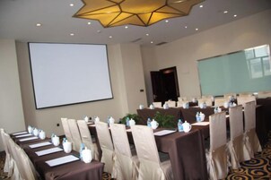 Un salón de conferencias con filas de mesas, sillas y una pantalla para proyector.