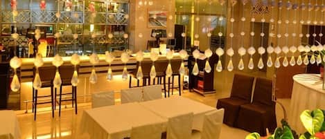 A restaurant with tables and chairs, hanging light fixtures, and a bar area.