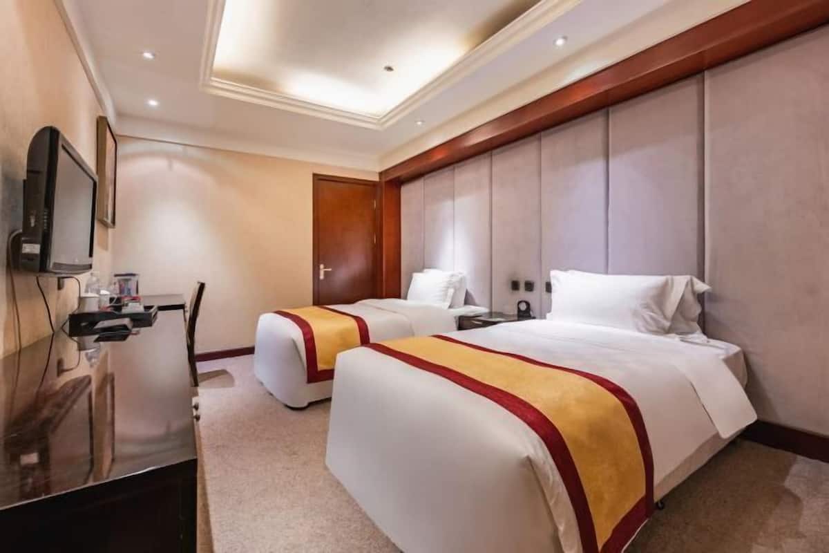 A hotel room with two beds, a TV, a desk, and a door.
