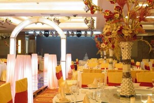 A banquet hall with round tables, chairs, and floral centerpieces.