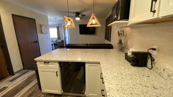 A kitchen with a granite countertop, white cabinets, a dishwasher, and a ceiling fan.