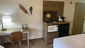 Habitación de hotel con cama, escritorio con lámpara, microondas, televisión y puerta.