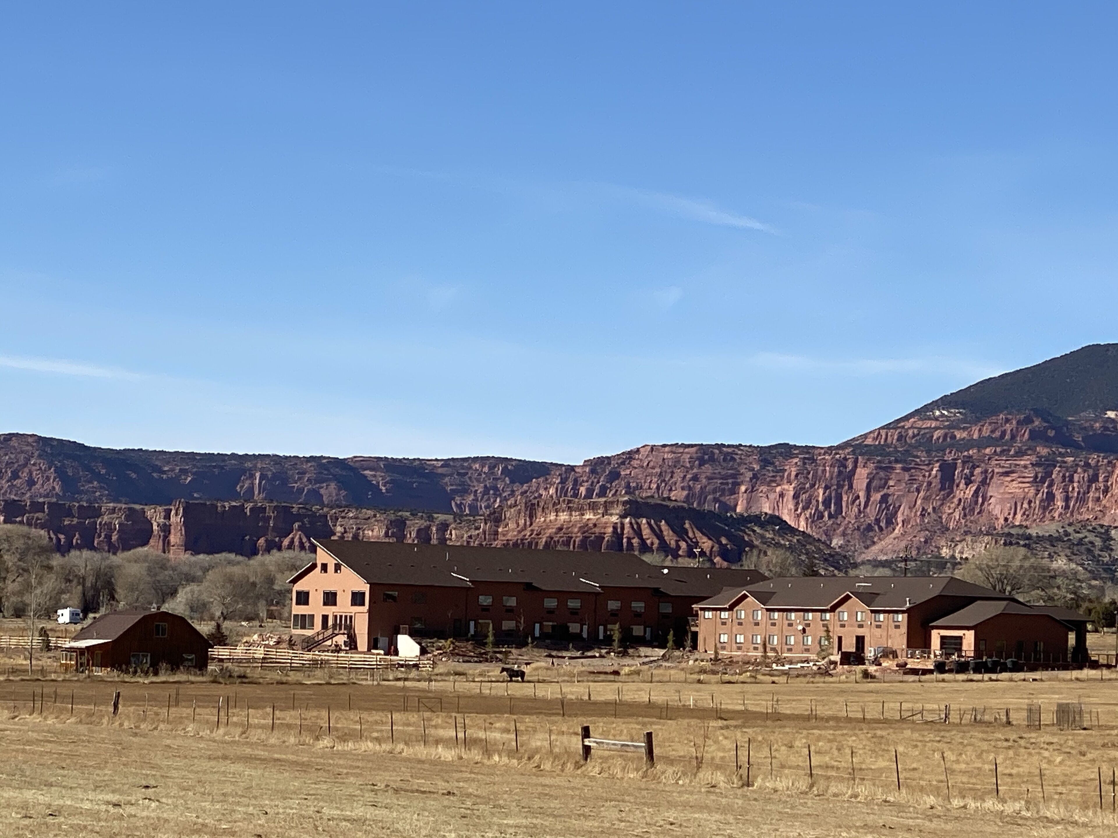 A residential area with multiple brick buildings, a fenced field, and a mountain backdrop.