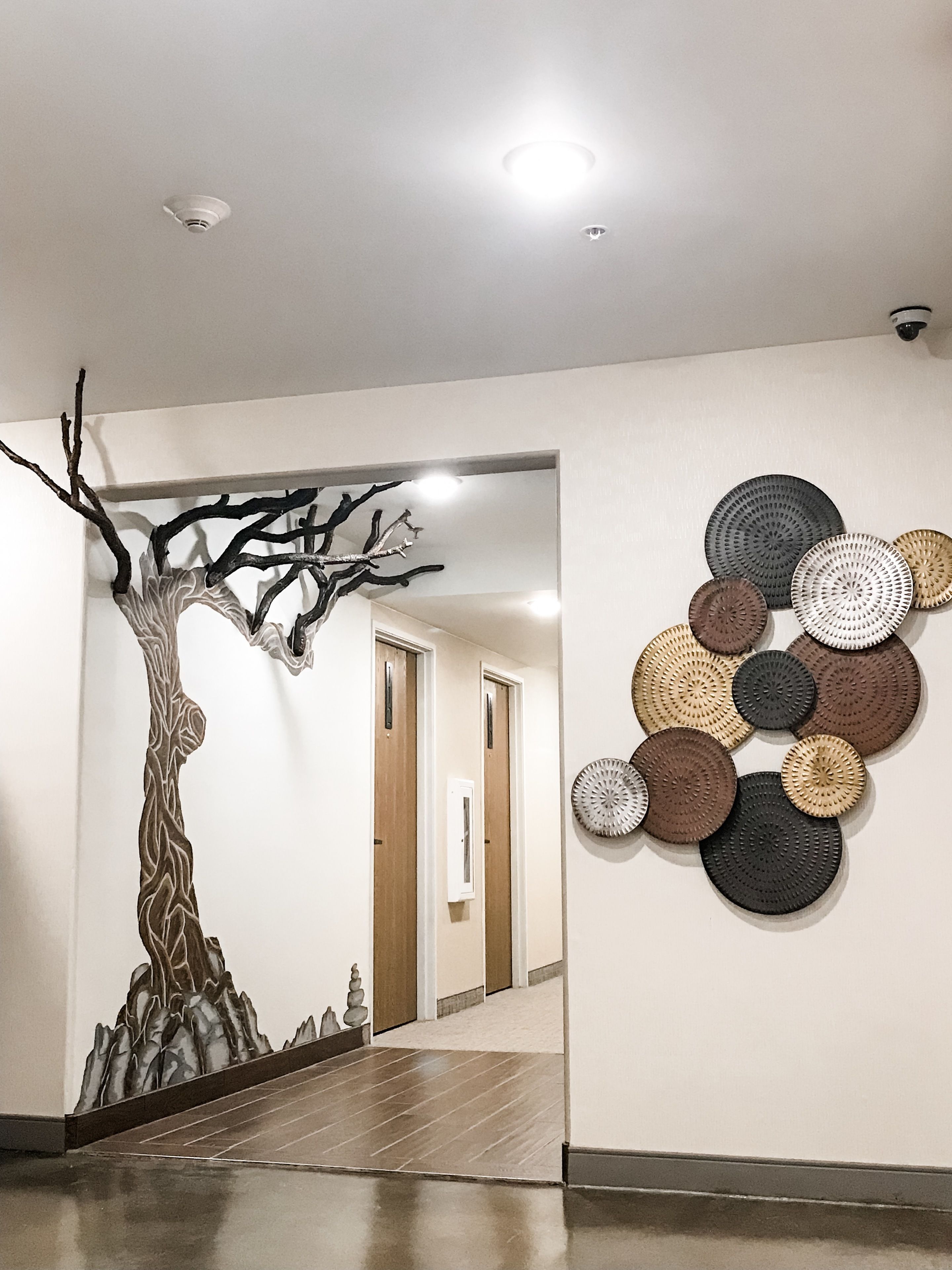 A hallway with a wall-mounted abstract art piece and a wall mural of a tree.