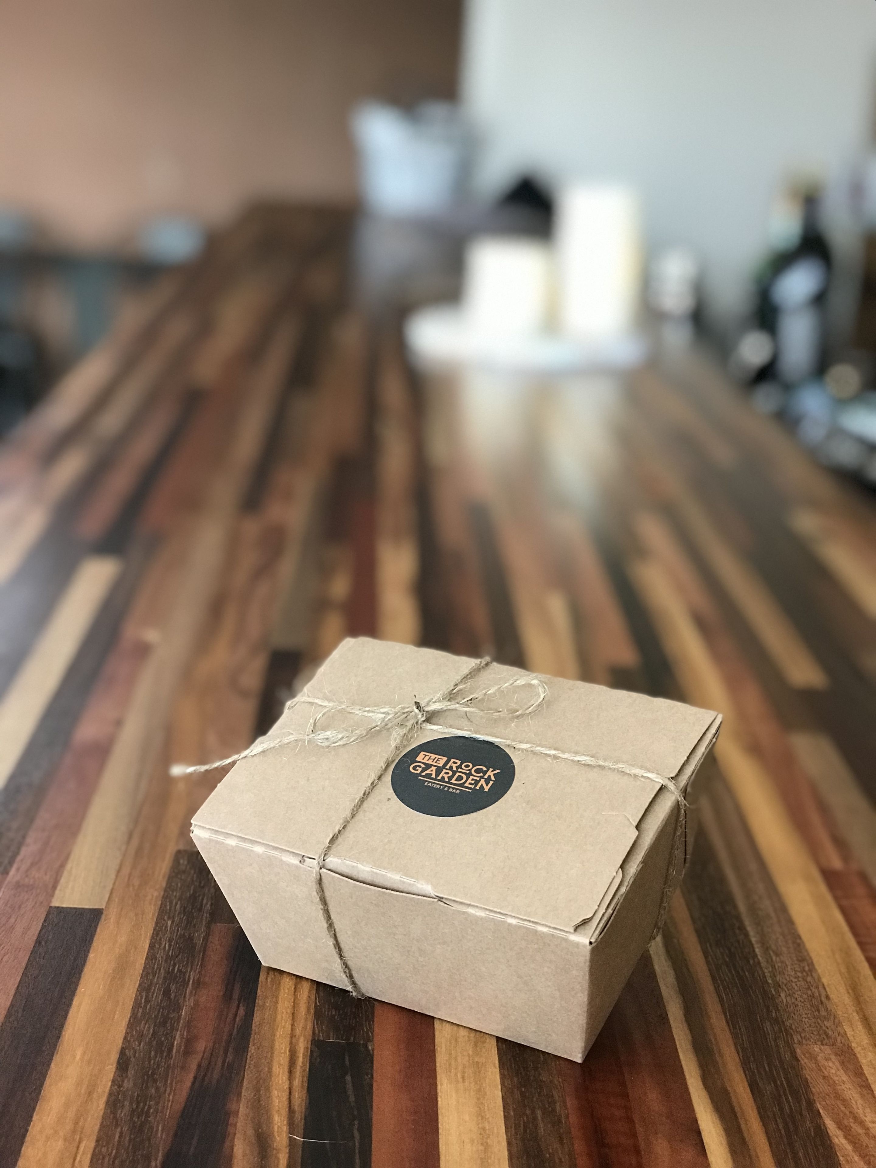 A small, square, cardboard box with a string and a label on a wooden table.