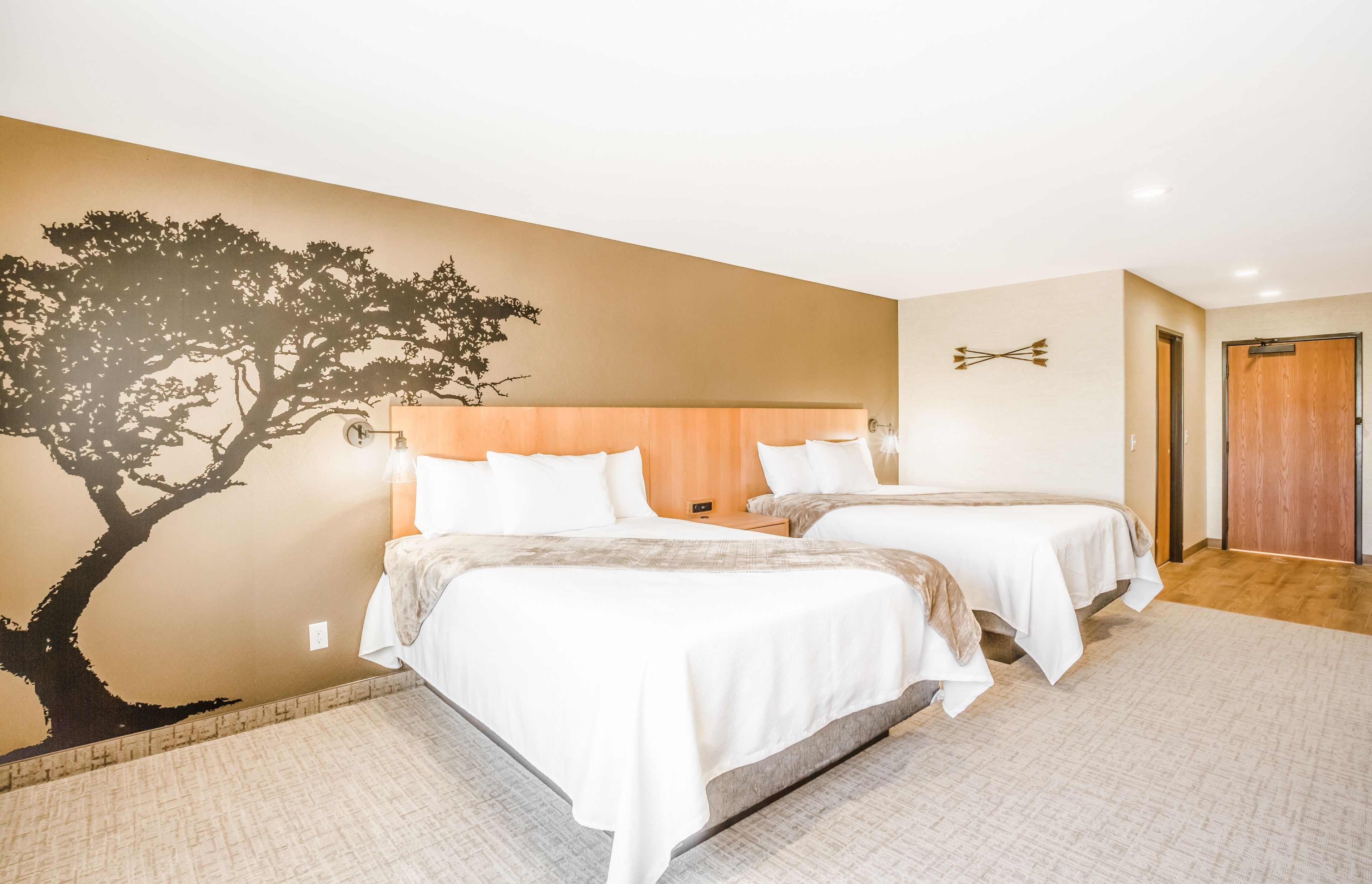 Een hotelkamer met twee bedden, een grote wanddecoratie van een boom en een houten hoofdbord.