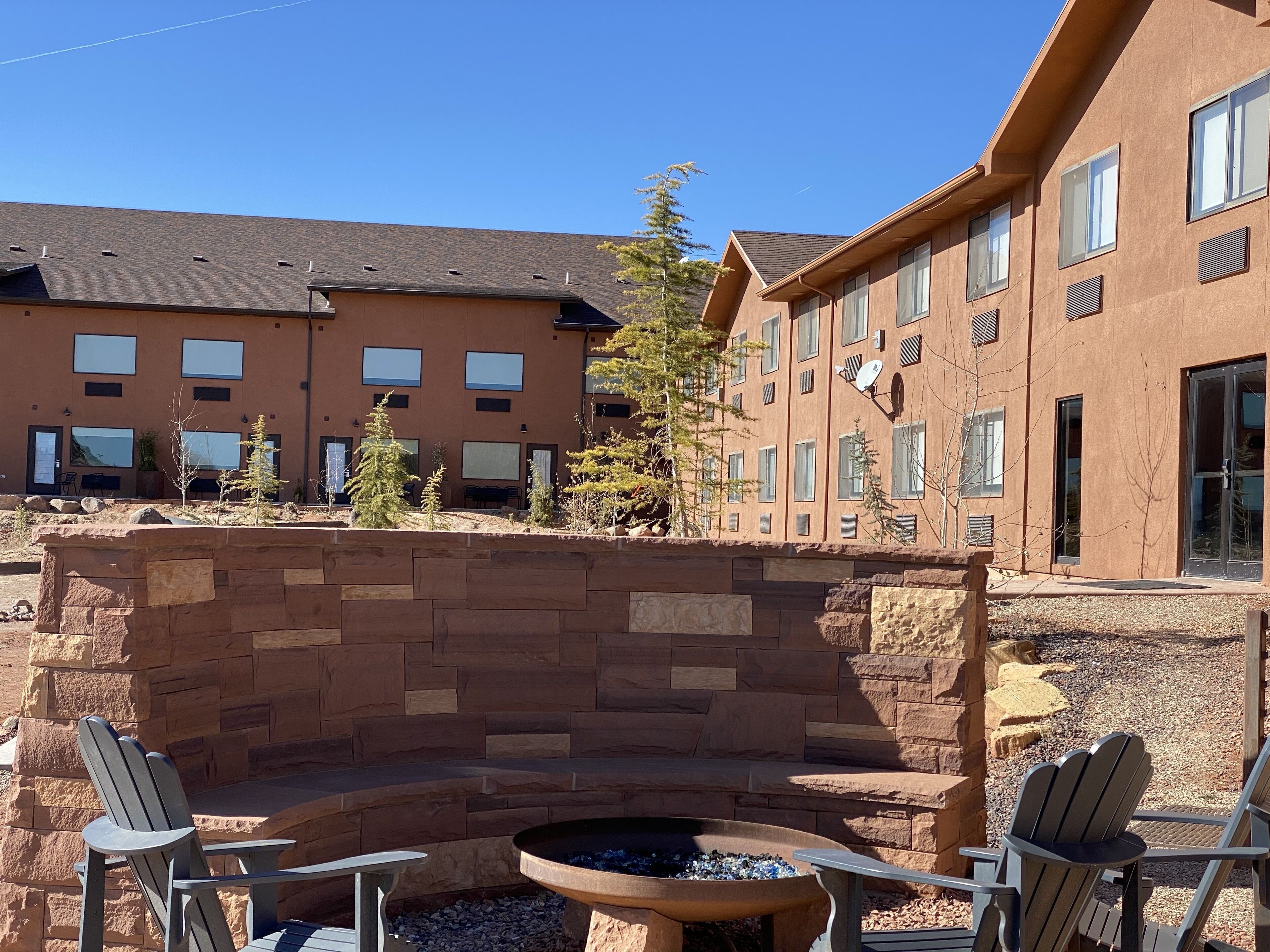 A courtyard with a fire pit, Adirondack chairs, and a stone wall.