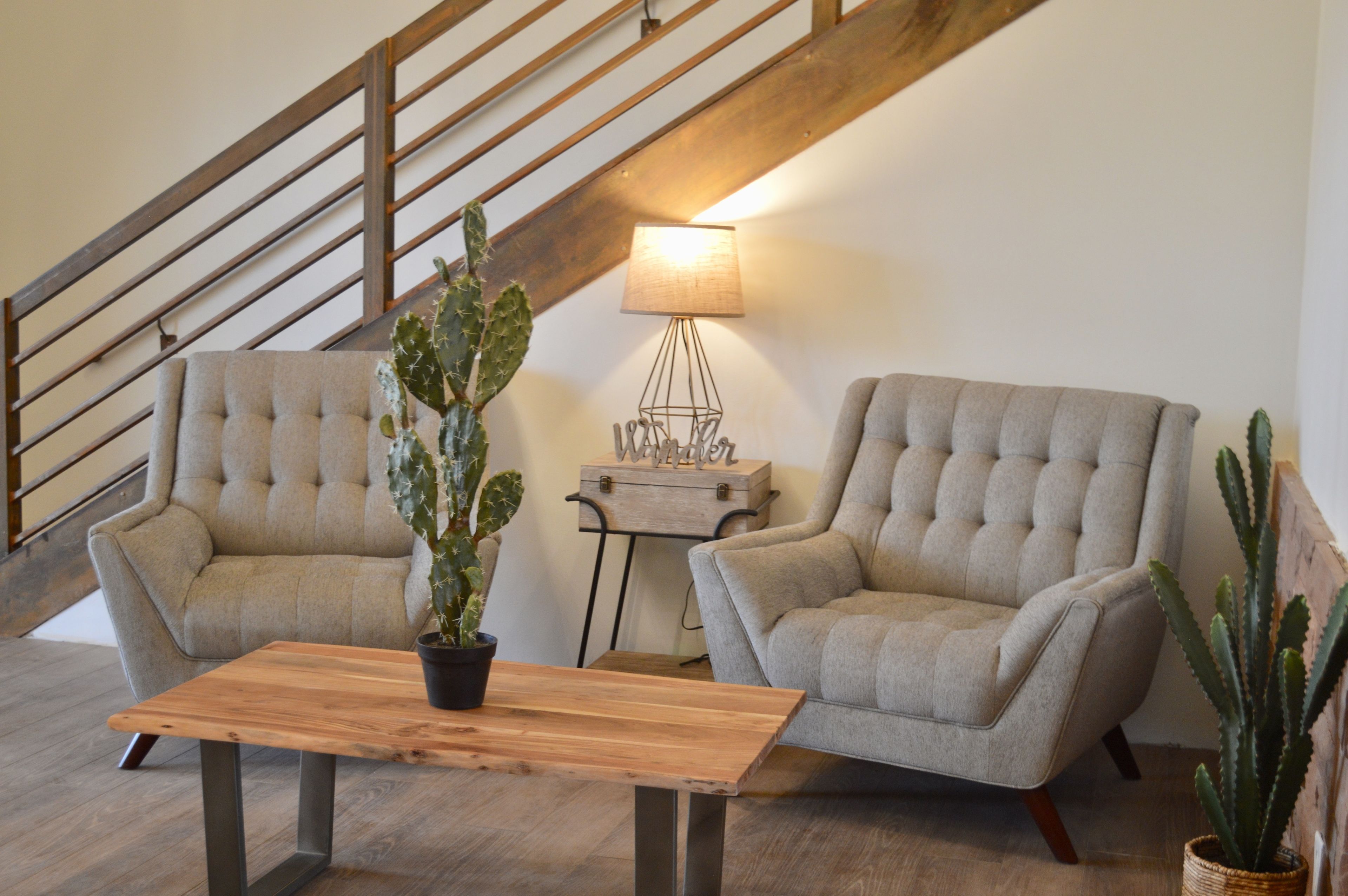 A living room with two beige armchairs, a wooden coffee table, a cactus plant, a lamp, and a small wooden side table.