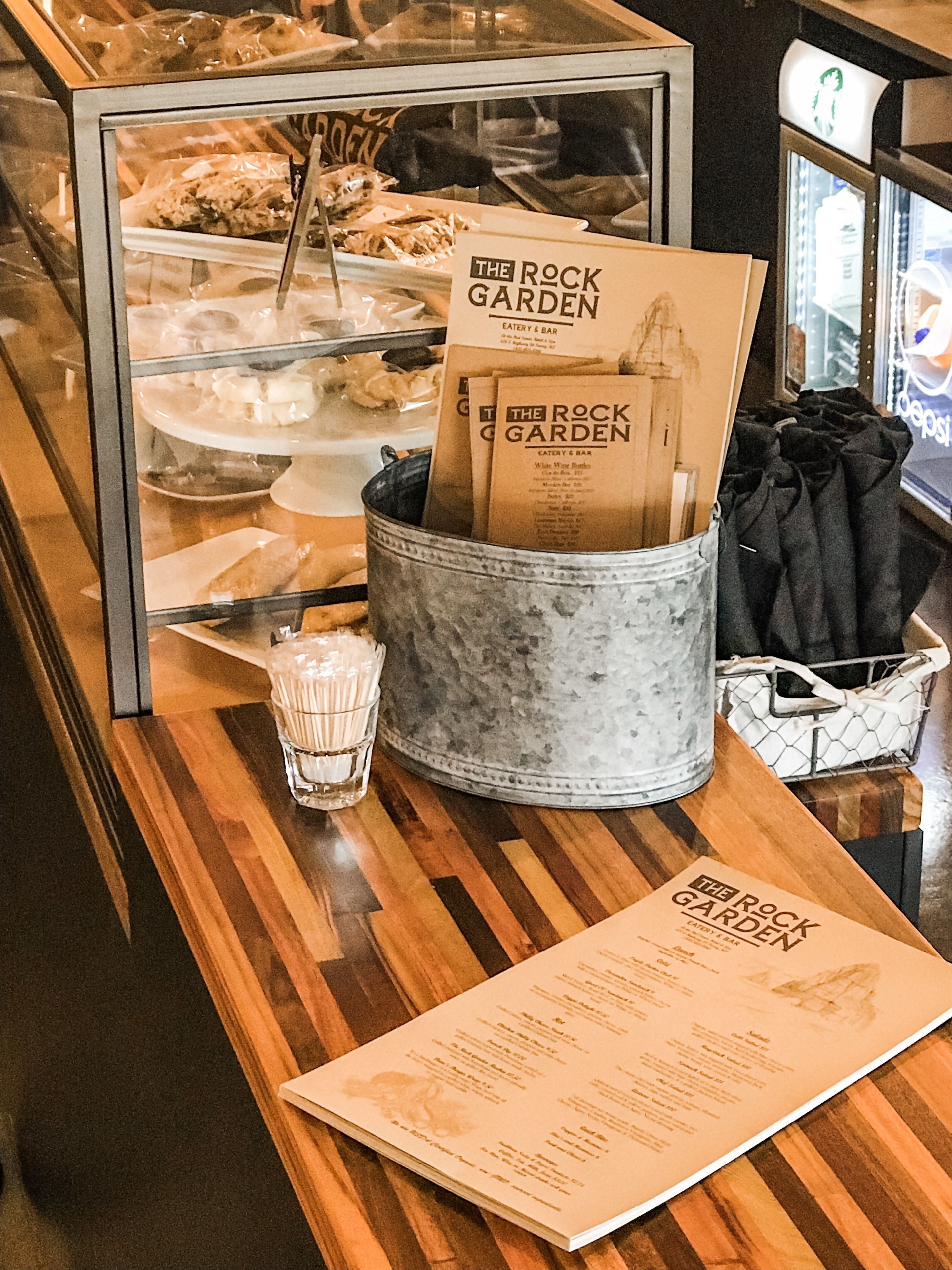 A menu stand with a menu, a glass of water, and a bucket with napkins at a restaurant.