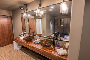 Un baño moderno con un espejo grande, tocador de madera y un lavabo de vidrio amplio.