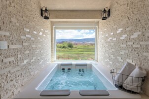 Un cuarto de spa con pared de piedra, un ventanal grande, una bañera de hidromasaje y dos luces empotradas.