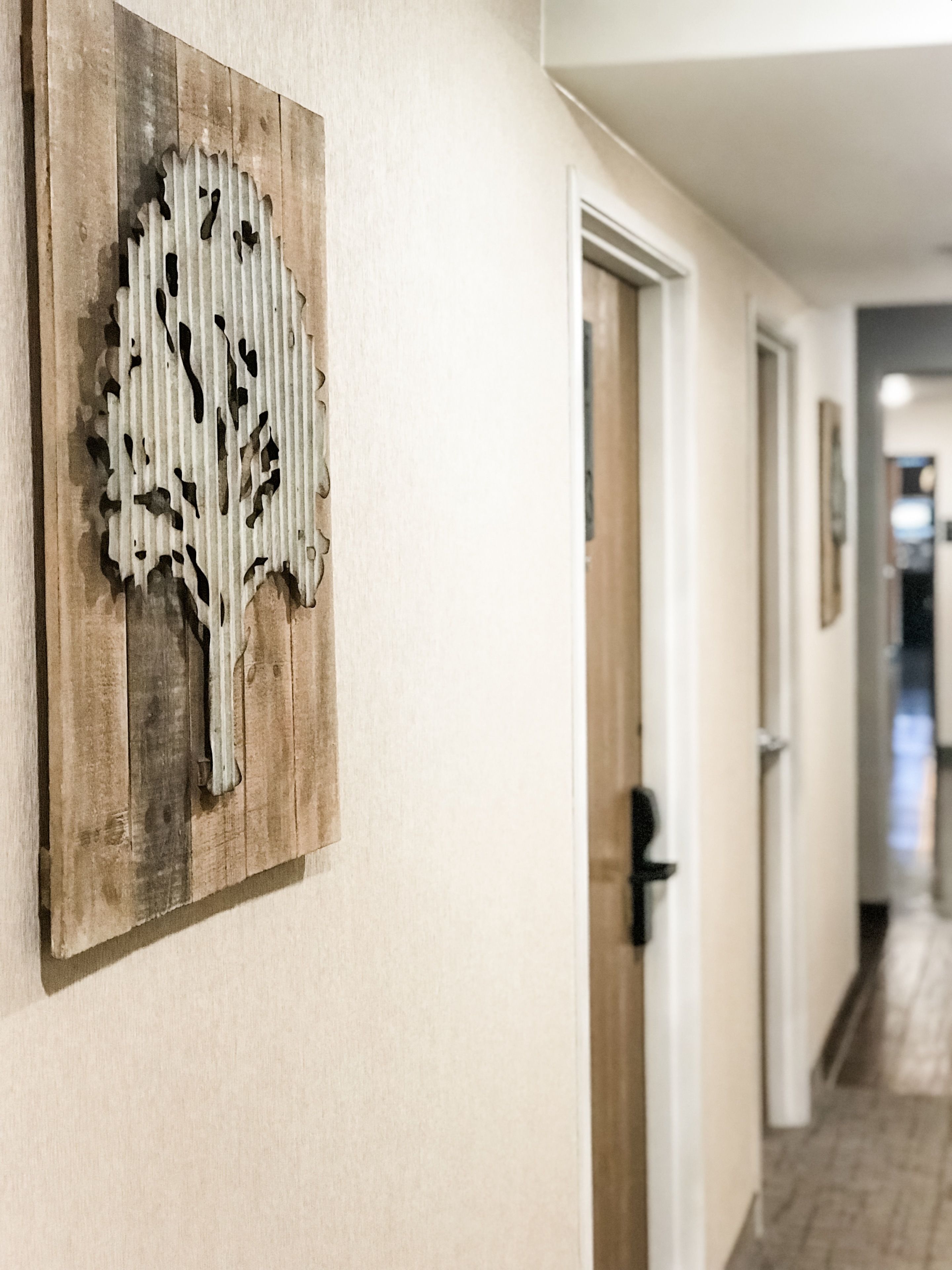 A hallway with a wooden wall art piece, a door, and a tiled floor.