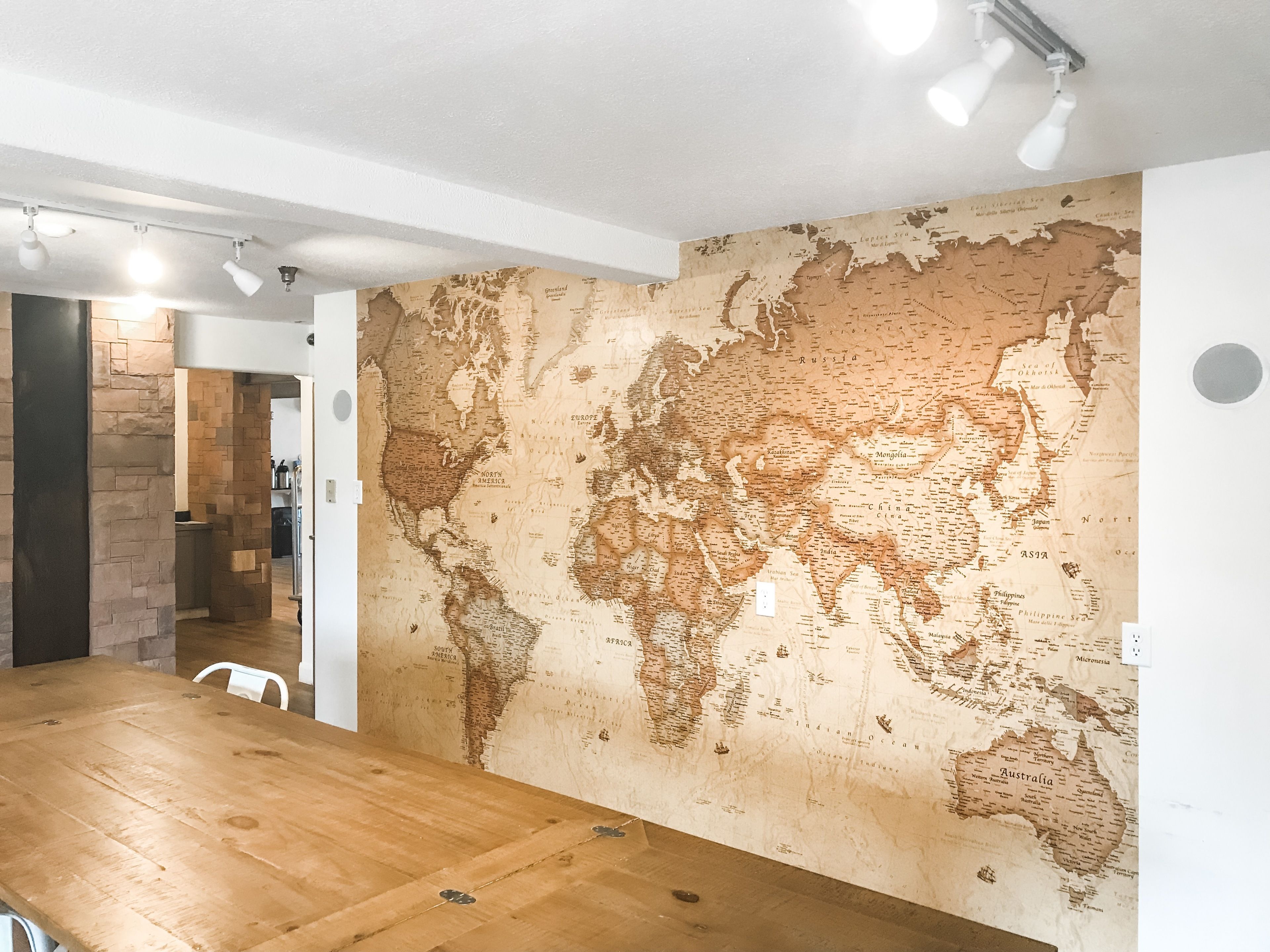 Una habitación con un gran mural de un mapa mundial en la pared, una mesa de madera para comer y un pilar de piedra.
