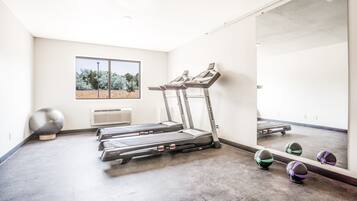 Un gimnasio con cintas de correr, un espejo grande y pelotas de ejercicio.