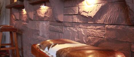 A stone wall with built-in lighting fixtures and a wooden bench with a cushion.