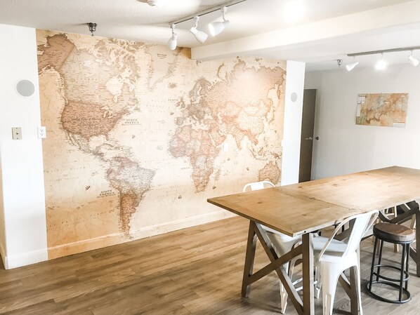 A room with a large world map mural, a wooden table, white chairs, and a modern ceiling light fixture. - Red Sands Hotel & Spa (Torrey)