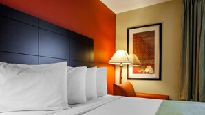 Habitación de hotel con una cama grande, un escritorio con silla, una lámpara y un cuadro en la pared.