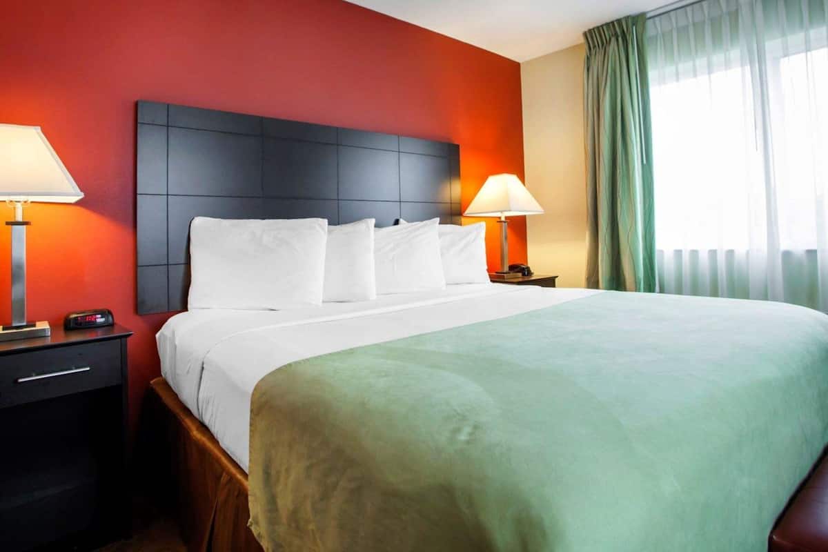 A hotel room with a large bed, two bedside tables, a nightstand, and a window with curtains.