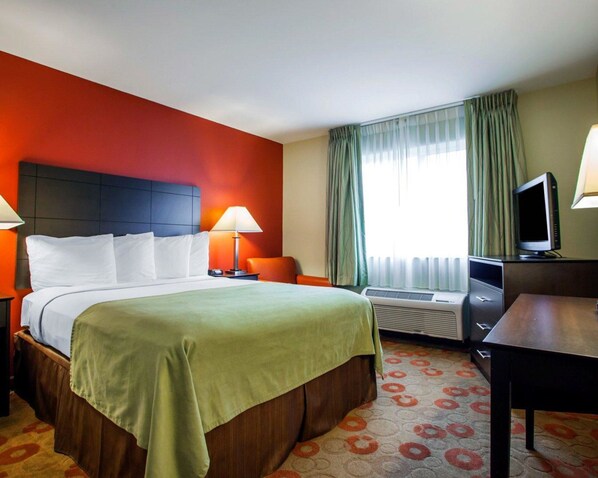 Habitación de hotel con cama, escritorio, televisión, lámpara y ventana con cortinas.