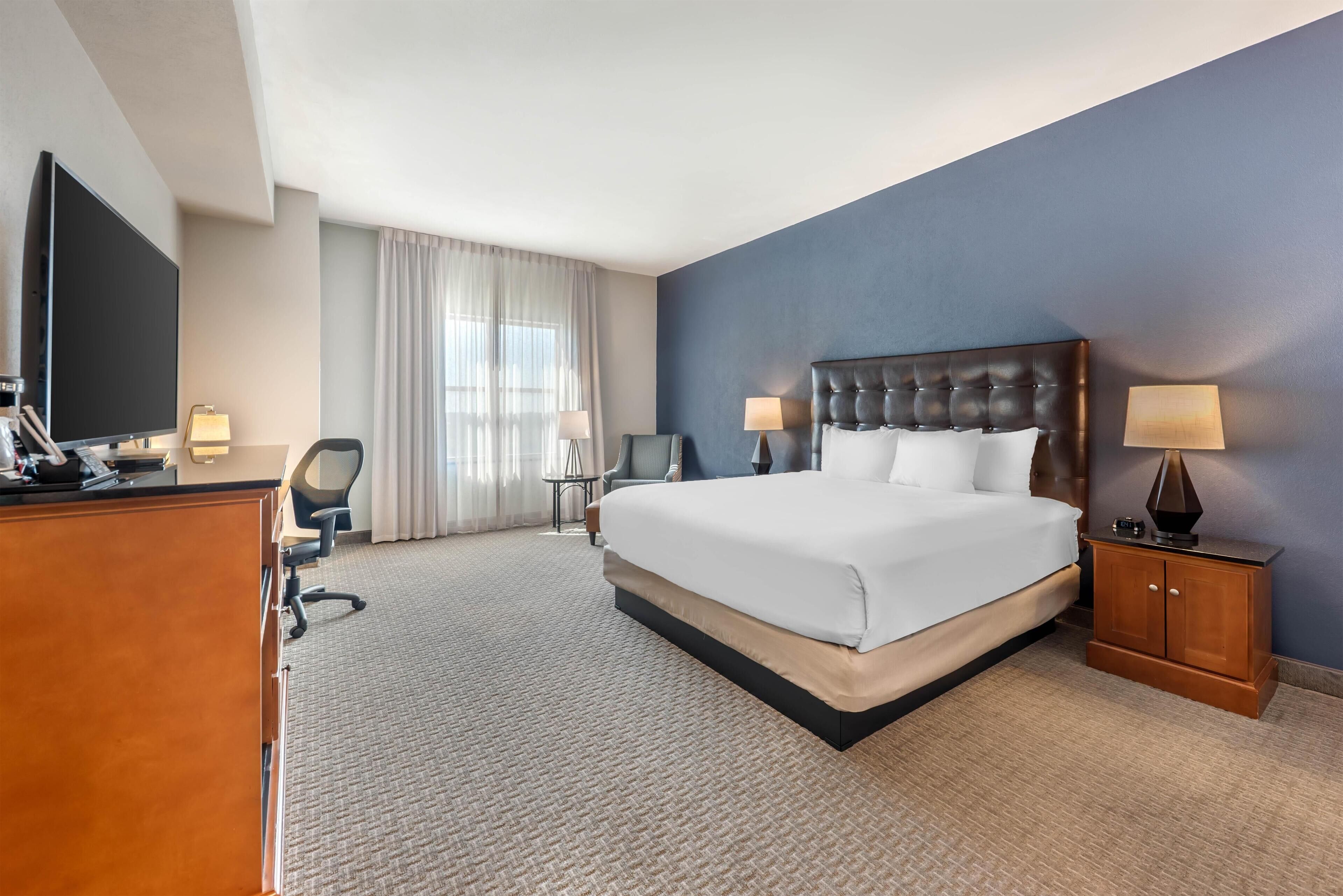A hotel room with a large bed, a desk, a TV, and a wardrobe.