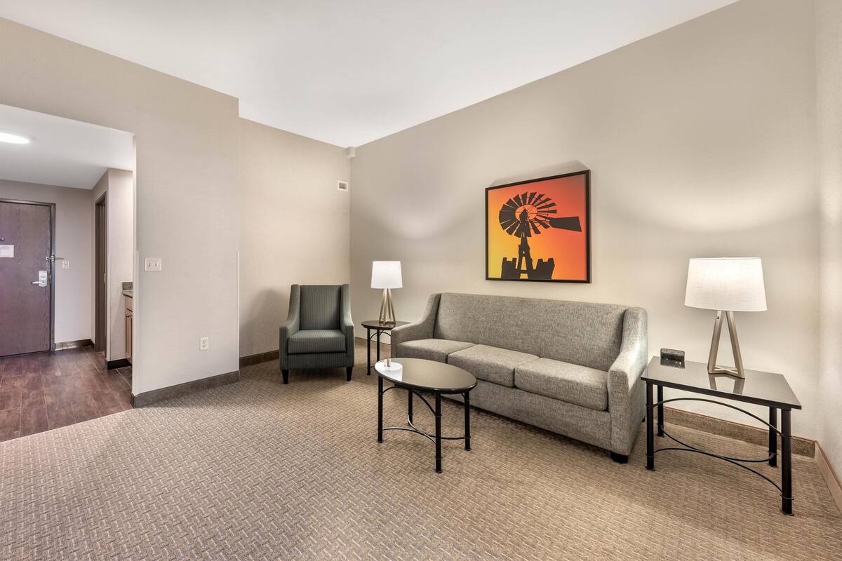 Une chambre d’hôtel avec un canapé gris, deux fauteuils, une petite table et une lampe.