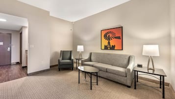 Habitación de hotel con un sofá gris, dos sillones, una mesita y una lámpara.