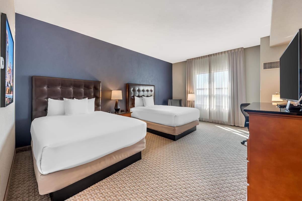 Une chambre d’hôtel avec deux lits, un bureau et une grande fenêtre avec des rideaux.
