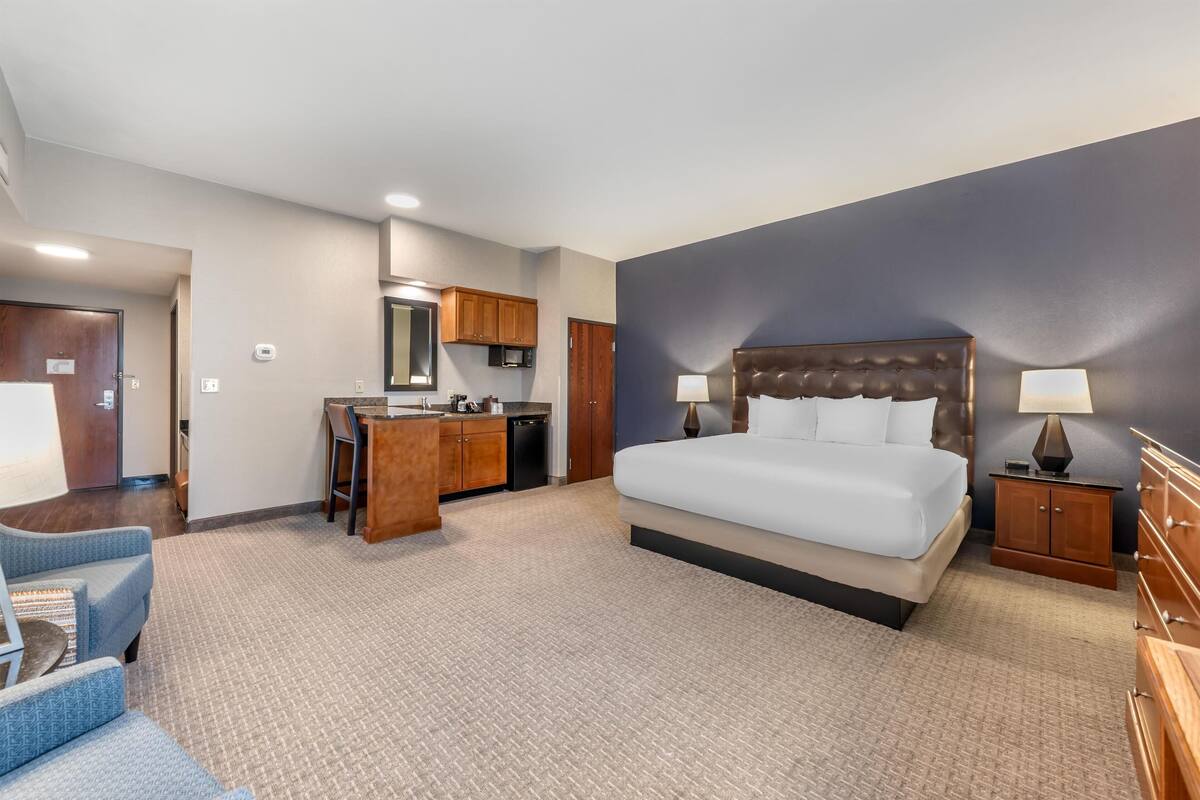 Une chambre d’hôtel avec un grand lit, un bureau avec une chaise, une kitchenette et une salle de bain.