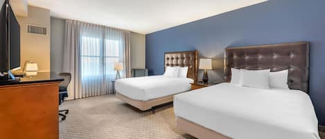 A hotel room with two beds, a desk, and a TV.