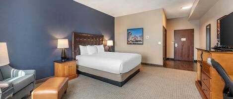 A hotel room with a large bed, a desk, a chair, a bench, a dresser, and a painting on the wall.