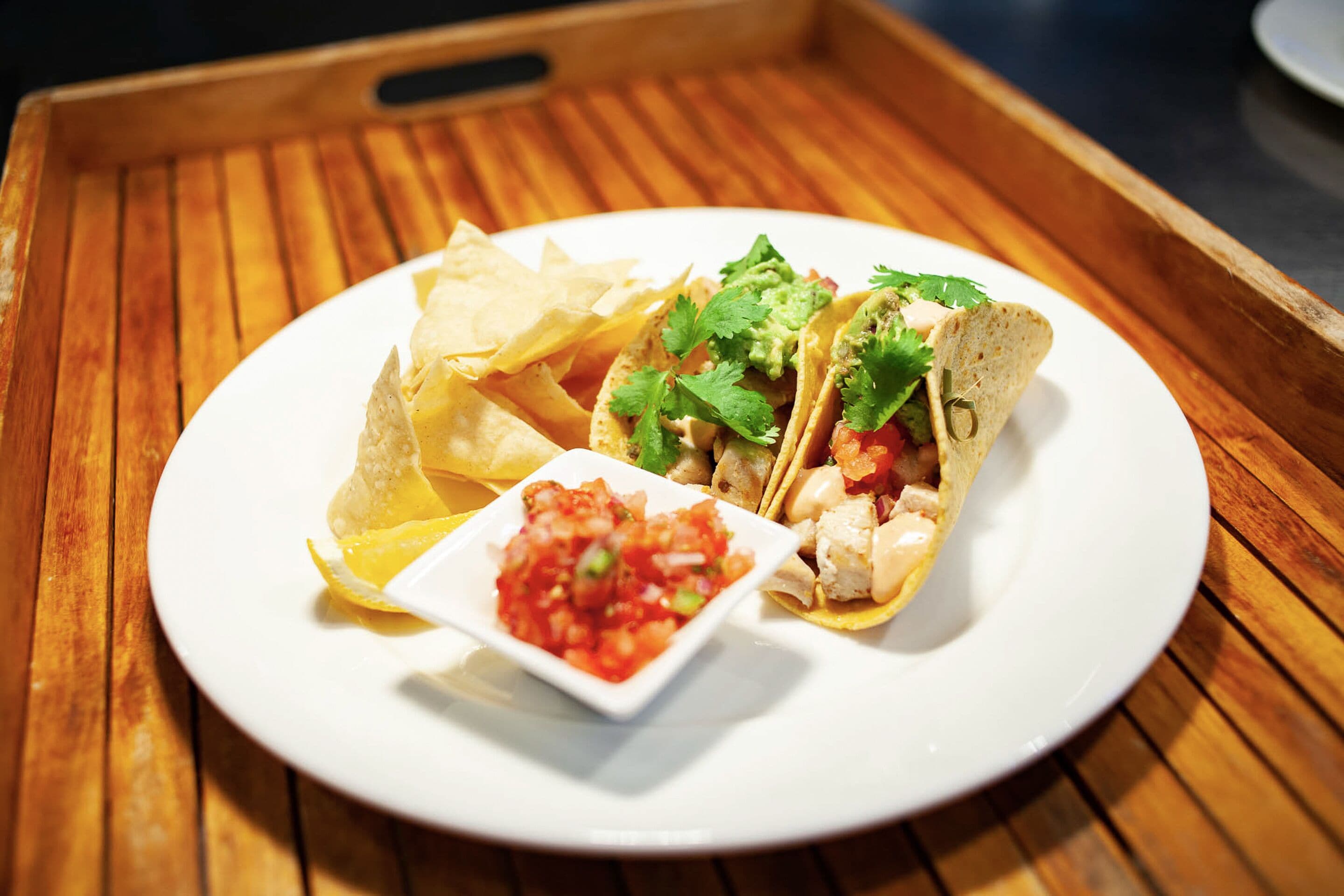 En tallerken med to tacos, en portion tortilla chips og en lille skål salsa.