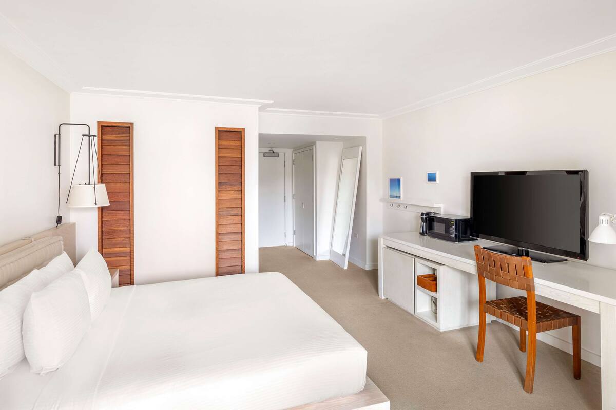 A hotel room with a bed, a desk with a television, a chair, and a wardrobe.